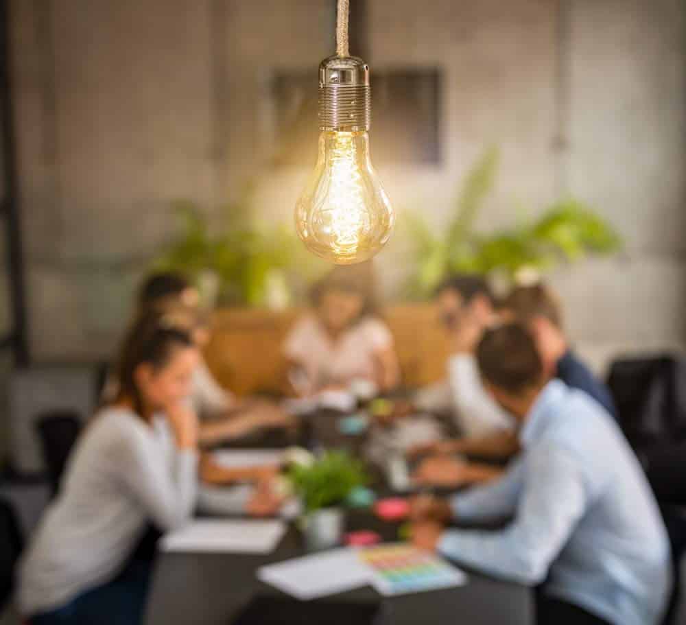 Image of a lightbulb with blurred images of co-workers collaborating in the background